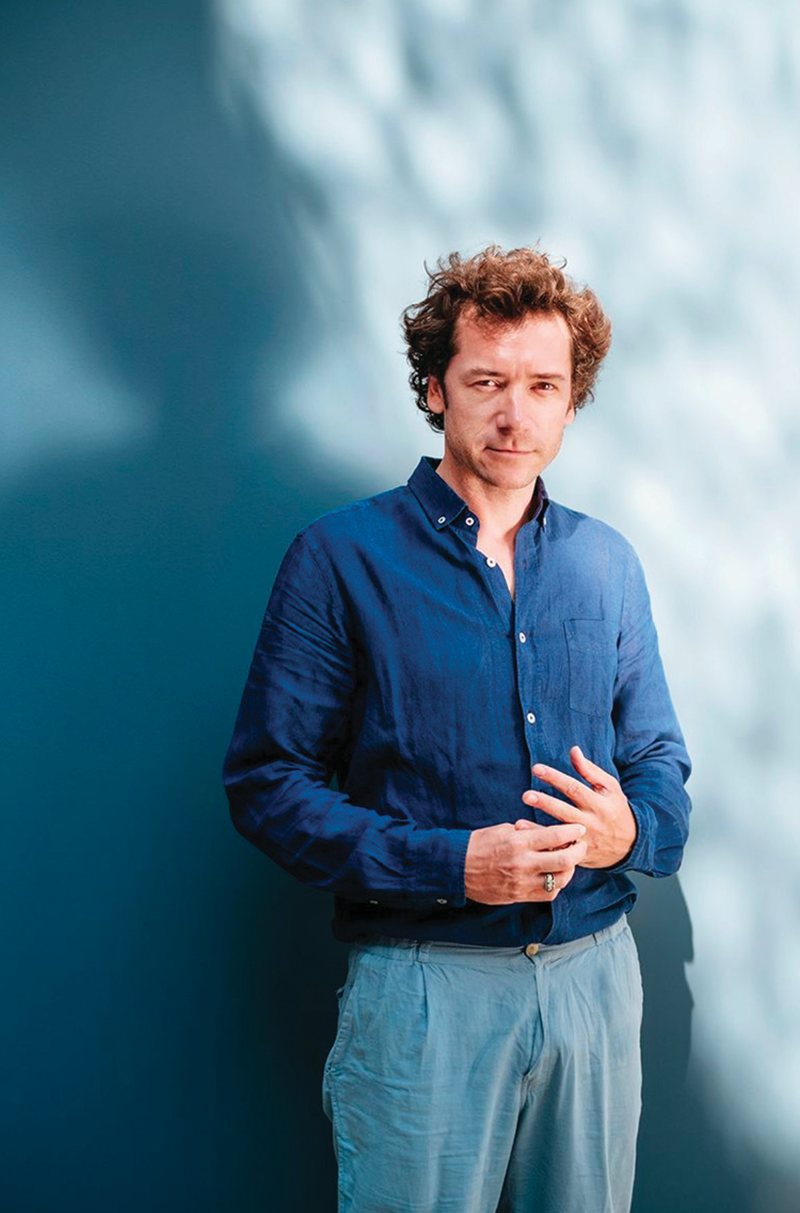 A journalist photographed against a blue wall